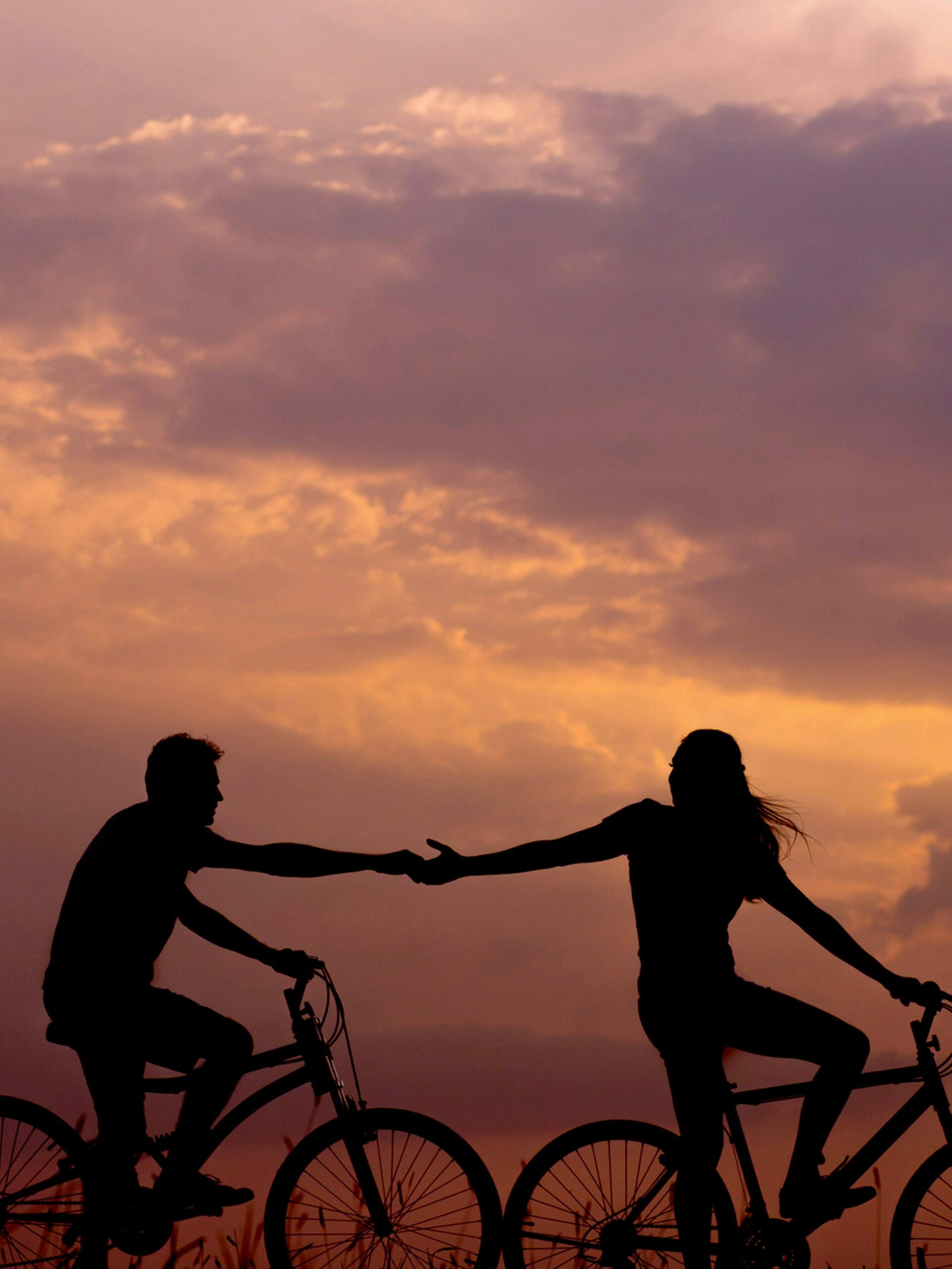 Partager son histoire d'amour une femme et un homme se tiennent la main à vélo. Cela illustre le fait qu'il est possible d'écrire un chapitre de sa vie relatant une rencontre amoureuse.